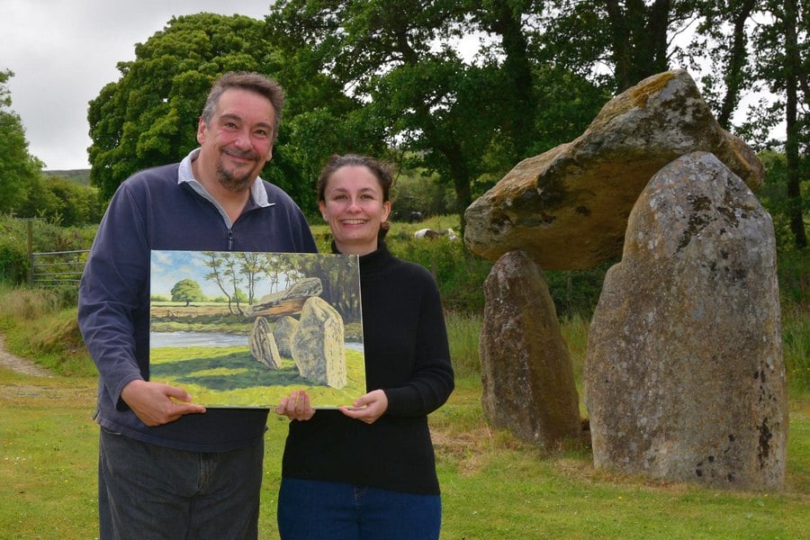 Happy client holding their landscape painting commission whilst standing in front of standing stones cromlech in Wales